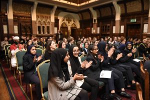 Young school pupils sat in chairs in ornate room, applauding