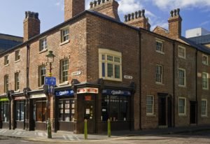 Corner shot of brick housing, shops on the bottom and private accomodation on first floor, chimneys and blue skies also seen